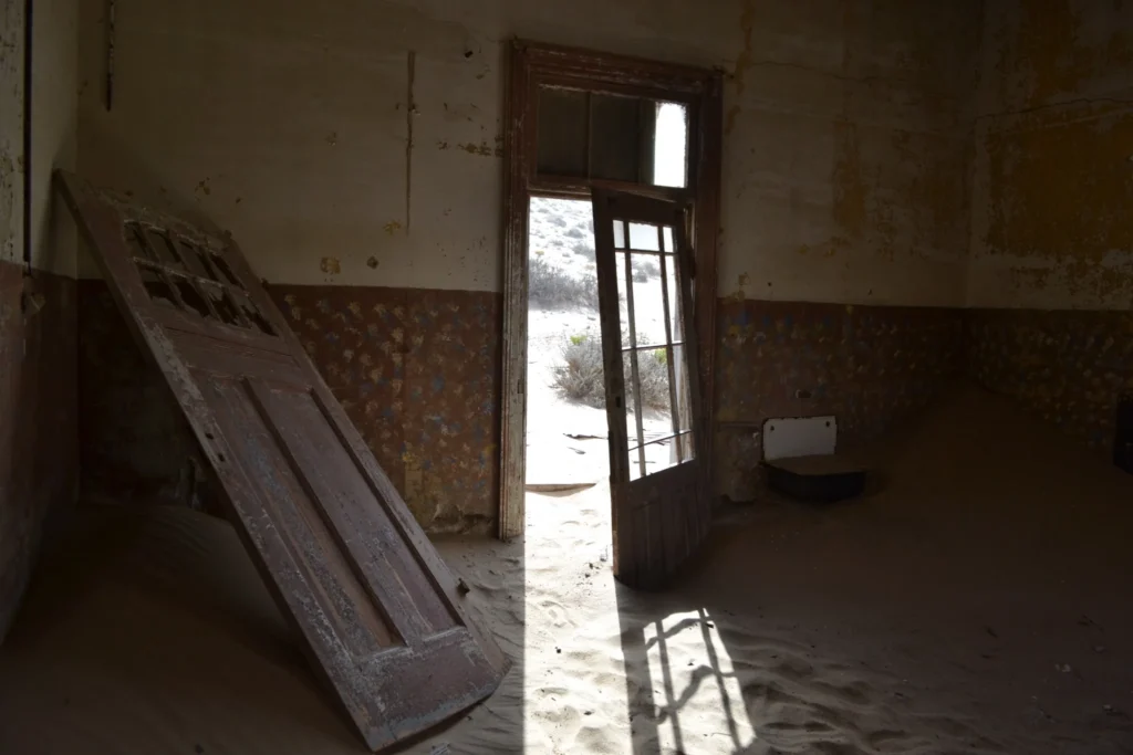 Dark abandoned interior at Kolmanskop with broken doors and sand on the floor