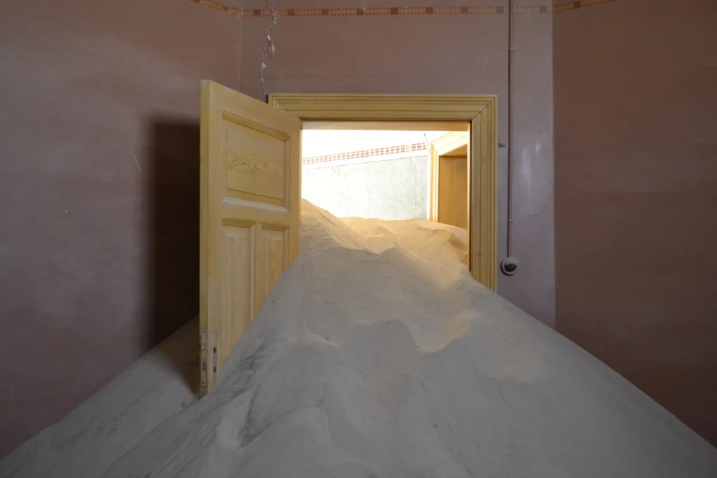 Large dune of sand pushing through an interior doorway at Kolmanskop Namibia