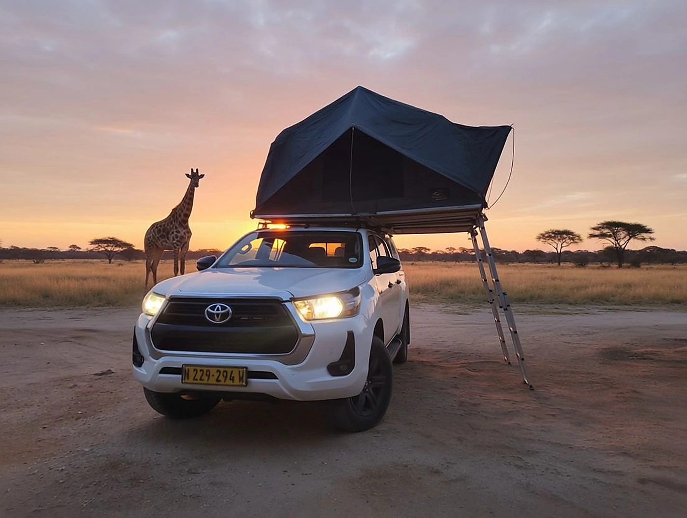 Toyota Hilux with rooftop tent beside a giraffe in Namibia at sunset